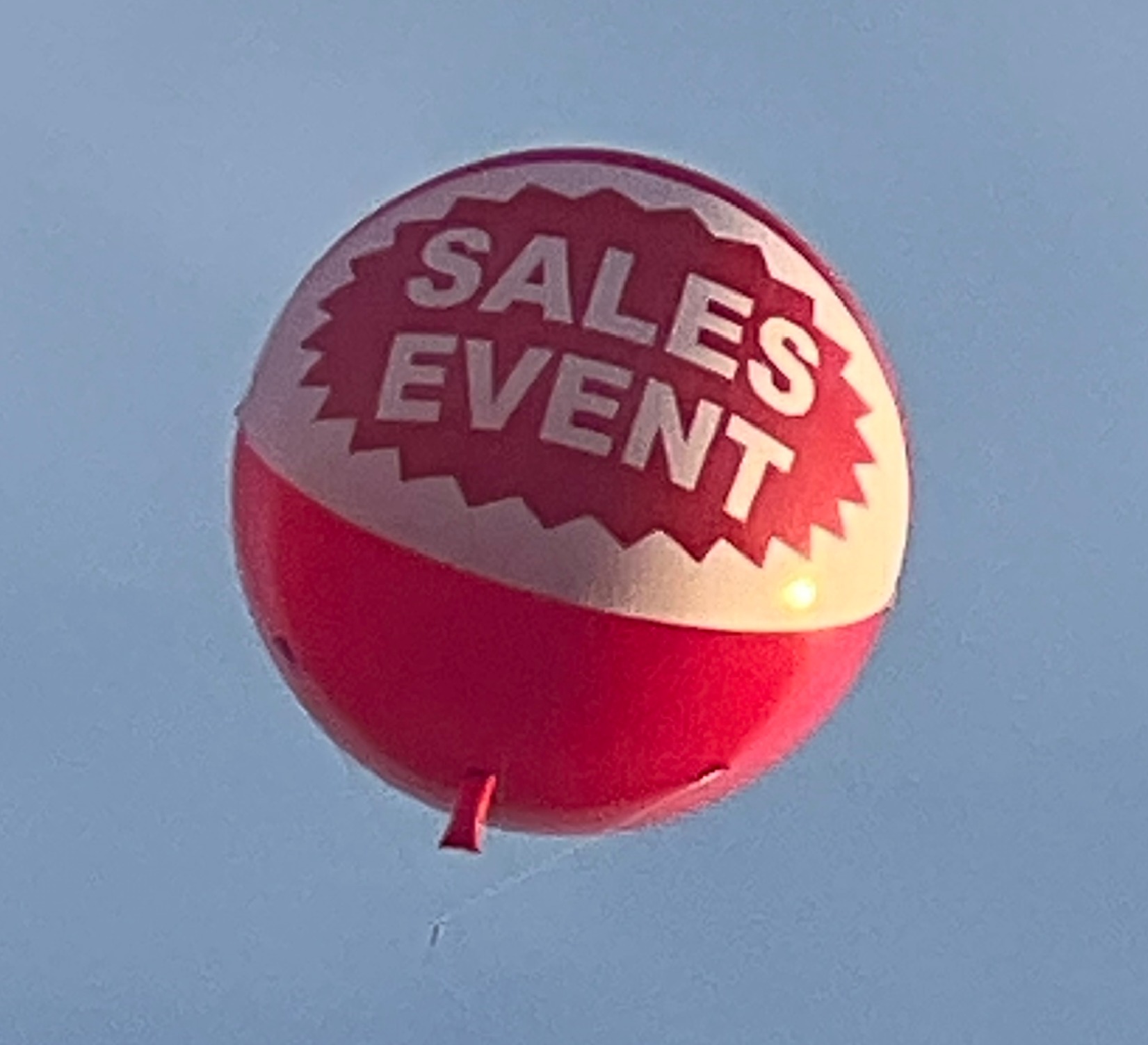 Red SALES EVENT helium advertising balloon over a car dealership
